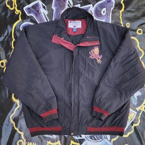 May include: A black Champion jacket with a maroon collar, cuffs, and hem. The jacket features a full zipper, snap closures, and the Arizona State University Sun Devils logo embroidered on the chest.