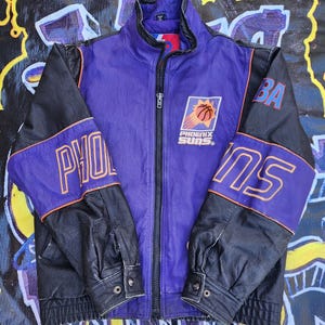 May include: A purple and black leather jacket with the Phoenix Suns logo and "PHX" and "SUNS" text on the sleeves.