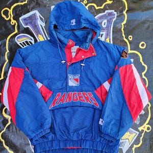 May include: A blue, red, and white New York Rangers Starter jacket. The jacket features a hood, the team logo, and the word "Rangers" in large letters across the front. The sleeves have red and white stripes.