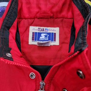 May include: Red Starter jacket with a black zipper and black trim. The jacket has a label that reads "Classic Team Collection NFL Starter America's Favorite Sport".