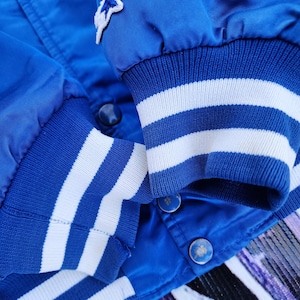 May include: Blue satin bomber jacket with white striped cuffs and a star-shaped patch on the left sleeve.