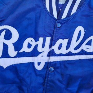 May include: A blue satin baseball jacket with a white "Royals" logo on the front.