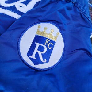 May include: A blue jacket with a white embroidered "R" with a gold crown and "KC" inside the "R".