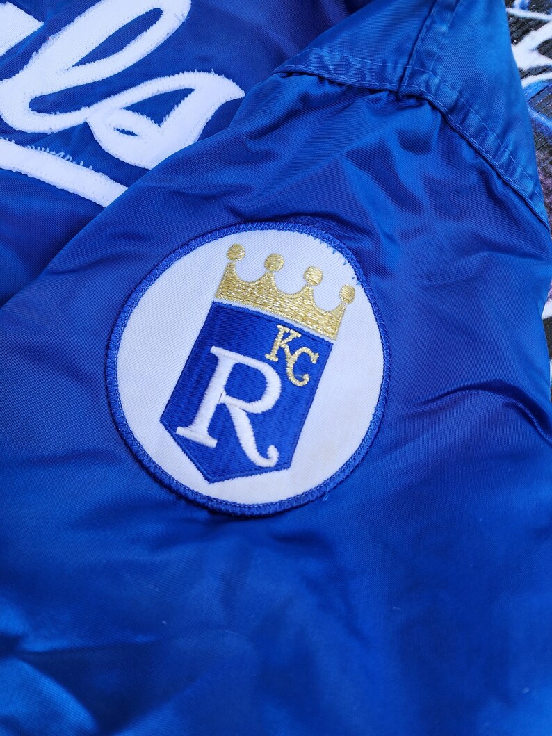 May include: A blue jacket with a white embroidered "R" with a gold crown and "KC" inside the "R".