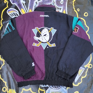 May include: A vintage Anaheim Ducks Starter jacket. The jacket is black, purple, and teal with the team logo on the back. The jacket has a full zip closure, a stand-up collar, and elastic cuffs. The Starter logo is visible on the chest.