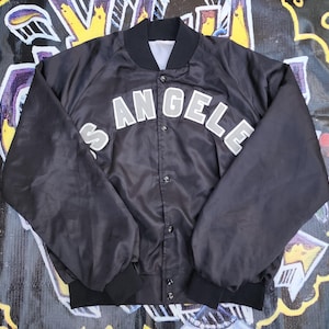 May include: A black satin bomber jacket with a silver embroidered "Los Angeles" design on the front.