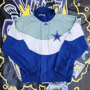 May include: A vintage windbreaker jacket in blue, white, and light green. The jacket features a full zipper, a high collar, and a star logo on the chest. The sleeves and lower portion are blue, with a white and light green panel across the chest.