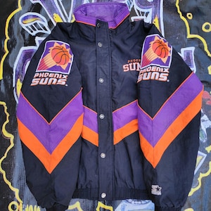 May include: Black, orange, and purple reversible jacket with the Phoenix Suns logo on both sides. The jacket has a zipper closure and a snap button placket. The jacket is made by Starter.