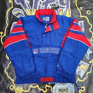 May include: Blue and red New York Rangers Starter jacket. The jacket features a blue body with red accents on the collar and sleeves. The word "Rangers" is embroidered across the chest.