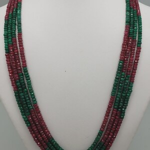 May include: A multi-strand necklace featuring alternating segments of faceted deep red and vibrant green beads. The necklace consists of five distinct strands that drape in a layered formation, secured at the top with metallic fasteners.