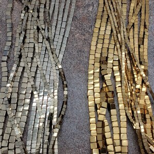 May include: Two strands of square-shaped beads, one strand is silver and the other is gold. The beads are arranged in a straight line and are all the same size.