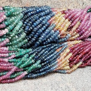 May include: A strand of faceted gemstone beads in shades of pink, green, blue, and yellow. The beads are all approximately the same size and shape, and they are strung together on a clear thread.