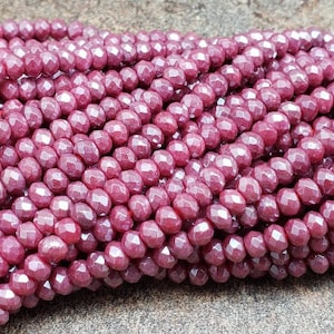 May include: A strand of deep red faceted glass beads. The beads are small and round, with a slightly irregular shape. They have a glossy finish.