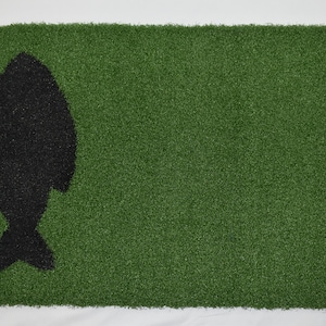 May include: A green artificial grass doormat with a black fish silhouette in the center.