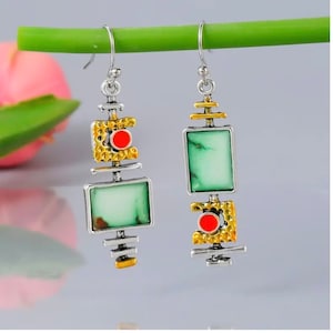 May include: A pair of silver and gold dangle earrings with green and red stone accents. The earrings feature a geometric design with square and rectangular shapes.