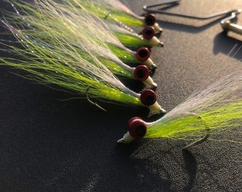 May include: A close-up of a row of eight green and white fly fishing lures with red eyes.