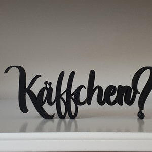 Könnte beinhalten: Schwarzes Holzschild mit dem Text "Kaffchen?" in einer stilisierten Schrift.