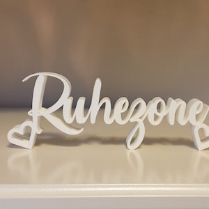 Könnte beinhalten: Ein weißes Holzschild mit dem Wort "Ruhezome" in kursivschrift, mit zwei kleinen weißen Herzen auf jeder Seite.