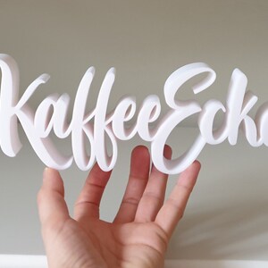 May include: White 3D sign that reads "Kaffee Ecke" in a cursive font.