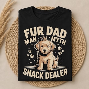 Peut inclure: Un t-shirt noir avec une illustration d'un chiot brun clair portant une petite couronne. Le texte FUR DAD, MAN MYTH et SNACK DEALER est imprimé en beige, entouré de petites empreintes de pattes et d'étoiles au centre du vêtement.
