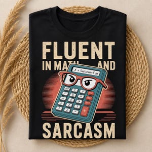 Peut inclure: Un t-shirt noir avec une illustration de calculatrice bleue portant des lunettes rouges. Le texte indique FLUENT IN MATH AND SARCASM avec X + Sarcasm = Fun sur l'écran. Un motif de coucher de soleil rouge se trouve derrière la calculatrice.
