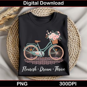 Peut inclure: Un t-shirt noir avec un vélo turquoise avec un panier de fleurs roses et blanches. Le texte "Flourish. Dream. Thrive" est imprimé sur le t-shirt.