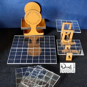 May include: A set of clear acrylic game tiles with a grid pattern. The tiles are stacked on top of each other. There is a wooden stand with a circular top that has the inscription "One Ring" on it. The stand is on a blue surface.