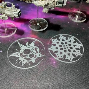 May include: Two white plastic bases with different designs. One base features a snowflake design, while the other has a more abstract design with a central circle and radiating lines. Both bases are circular and have a smooth, glossy finish.