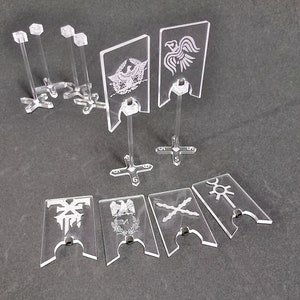 Könnte beinhalten: Ein Satz aus klaren Acryl-Flaggenständern mit verschiedenen Designs, darunter ein Vogel, ein Kreuz und eine Sonne. Die Ständer sind von 1 bis 6 nummeriert.