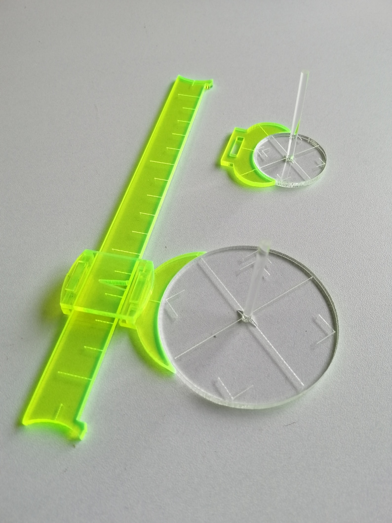 May include: Two clear plastic protractors with a green ruler. The protractors have a center point with lines radiating out to the edge of the circle. The ruler has a green handle and a clear plastic ruler with markings.