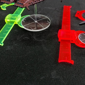 May include: Two clear plastic rulers with a green and red color scheme. The rulers are marked with measurements and have a curved edge. The rulers are on a black surface.