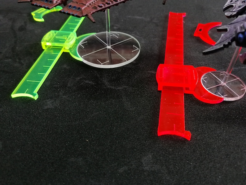 May include: Two clear plastic rulers with a green and red color scheme. The rulers are marked with measurements and have a curved edge. The rulers are on a black surface.