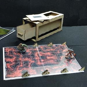 Può includere: Una scatola di legno con un cassetto e un coperchio rimovibile. La scatola è aperta e il cassetto è tirato fuori. La scatola è appoggiata su una superficie nera con un tabellone da gioco rosso e nero e figure in miniatura.