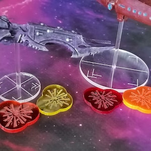 Peut inclure: Deux vaisseaux spatiaux miniatures sur des socles en plastique transparent avec des jetons d'effet d'explosion rouge, orange et jaune. Le vaisseau spatial de gauche est noir et gris avec un design pointu et angulaire. Le vaisseau spatial de droite est brun avec un design plus arrondi.