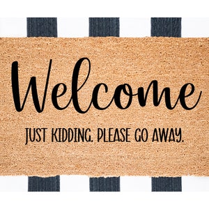 May include: A brown coir doormat with the text "Welcome" in a black cursive font. Below the word "Welcome" is the text "Just kidding. Please go away." in black.