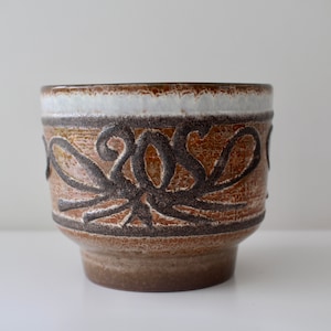 May include: A brown ceramic planter with a white rim and a decorative design of brown and black swirls.