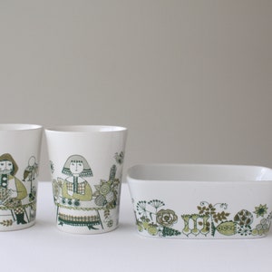 Op de afbeelding: Set van drie witte keramische bekers en een rechthoekige schaal met een groen en bruin bloemenpatroon. De bekers hebben illustraties van mensen in traditionele kleding.