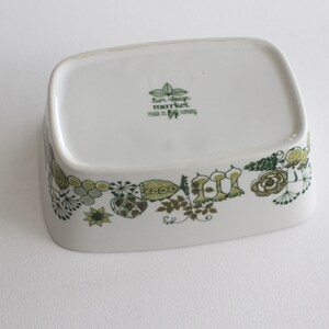 Op de afbeelding: Witte keramische serveerschaal met een groen en bruin bloemenontwerp rond de rand. De onderkant van de schaal heeft de tekst "tur-design market made in Denmark".