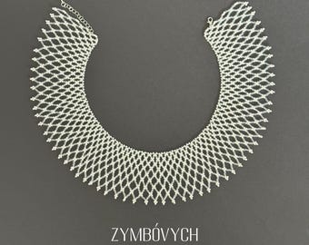 May include: A white beaded choker necklace with a geometric design. The necklace is made of small, white beads that are strung together in a pattern of diamonds. The necklace is a statement piece that would be perfect for a special occasion.