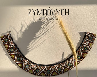 Könnte beinhalten: Eine farbenfrohe Perlenkette mit einem geometrischen Muster in den Farben Schwarz, Weiß, Rot, Gelb und Grün. Die Kette ist gebogen und hat einen Verschluss. Der Text "ZYMBÓVYCH -art studio- " ist über der Kette sichtbar.