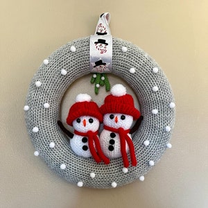 May include: A gray knitted wreath with white pom-poms and two crocheted snowmen with red hats and scarves.