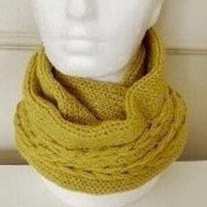 May include: A mustard yellow knitted infinity scarf. The scarf is made of a soft, chunky yarn and has a simple, cable knit pattern.