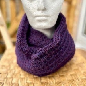 Könnte beinhalten: Ein violetter gestrickter Infinity-Schal. Der Schal ist aus weichem, strukturiertem Garn gefertigt und perfekt, um sich im Winter warm zu halten.