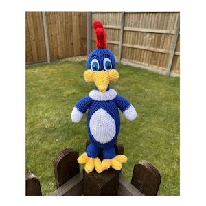 Könnte beinhalten: Ein blauer und weißer gestrickter Spielzeugvogel mit roter Haube und gelben Füßen. Der Vogel hat große blaue Augen und einen gelben Schnabel.