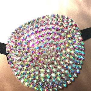 May include: A pink eye patch covered in iridescent rhinestones. The patch has a black elastic strap.