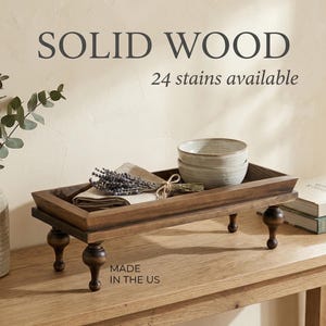 May include: A rectangular, solid wood serving tray with four turned legs. The tray is stained a dark brown and holds two light-colored bowls, a folded linen napkin, and a bundle of dried lavender. Text on the image reads "SOLID WOOD" and "24 stains available."