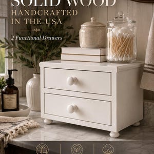 May include: A white solid wood storage unit with two functional drawers and round knobs, standing on four small ball feet. The text on the image reads: SOLID WOOD, HANDCRAFTED IN THE USA, 2 Functional Drawers, BOW-WRAPPED GIFT READY, OKEO-TEX CERTIFIED, 100% COTTON.