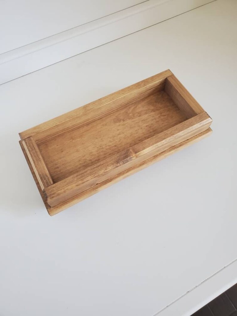 Pode incluir: Uma bandeja retangular de madeira com acabamento castanho claro. A bandeja tem uma borda elevada e um interior rebaixado. O gr&atilde;o da madeira &eacute; vis&iacute;vel, adicionando textura. Provavelmente usado para servir ou organizar itens.