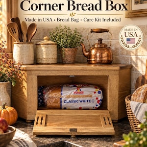 May include: A solid wood corner bread box with a drop-down front door. The text on the box reads Solid Wood Corner Bread Box, Made in USA, Bread Bag + Care Kit Included. A loaf of Wonder Classic White bread is stored inside the wooden container.