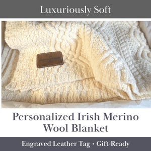 May include: Cream-colored Irish Merino wool blanket with a cable knit design. The blanket has a leather tag with text. The words "Luxuriously Soft" are at the top of the image, and "Personalized Irish Merino Wool Blanket" is at the bottom.